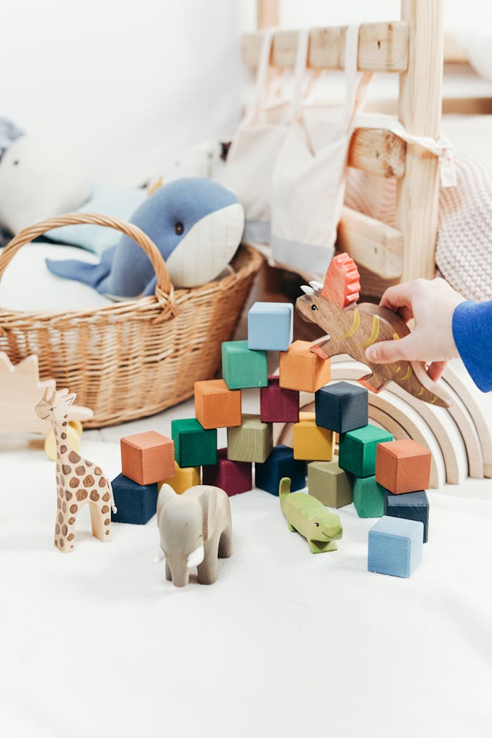 Home A child's hand arranges colorful wooden toys and animal figures on a playroom floor.